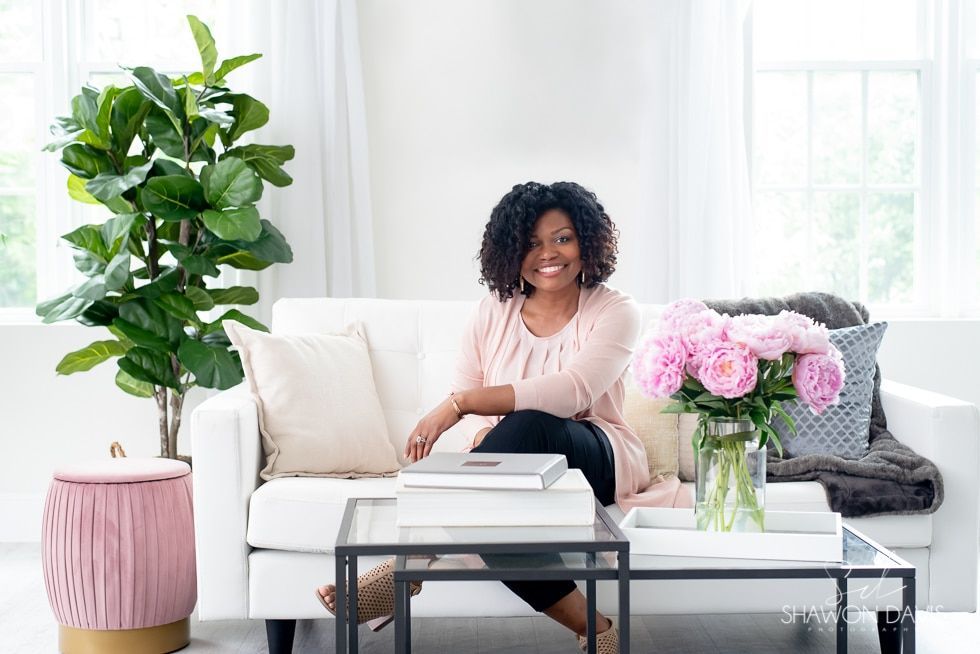 Woman sitting on a white sofa in a bright living room with flowers, plants, and a coffee table