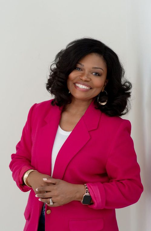 Smiling woman in a bright pink blazer posing against a light gray background