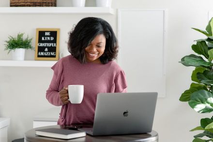 Person smiling at a laptop while holding a mug in a bright home office