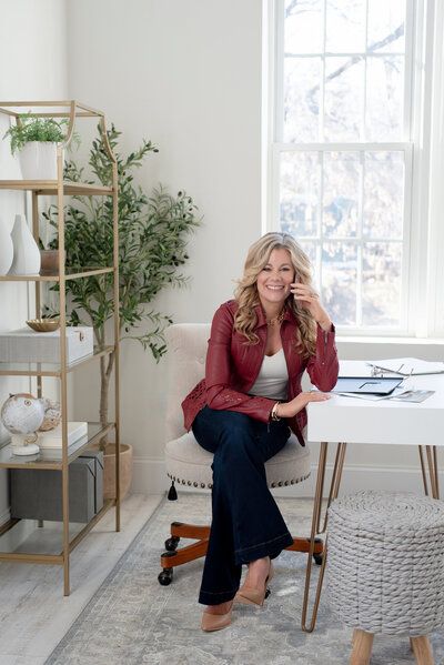 Woman sitting at a white desk in a bright home office with plants and a window