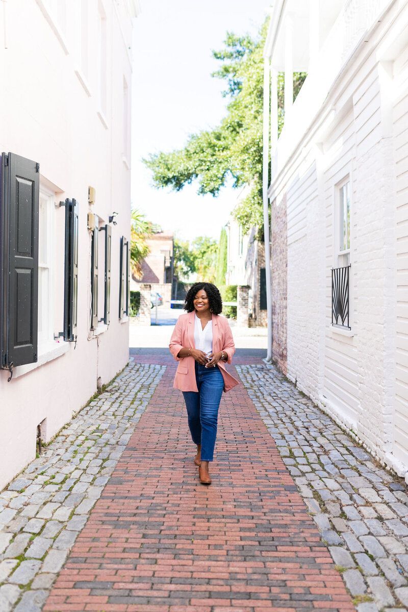 Person walking down a brick alley between white buildings, holding a jacket.