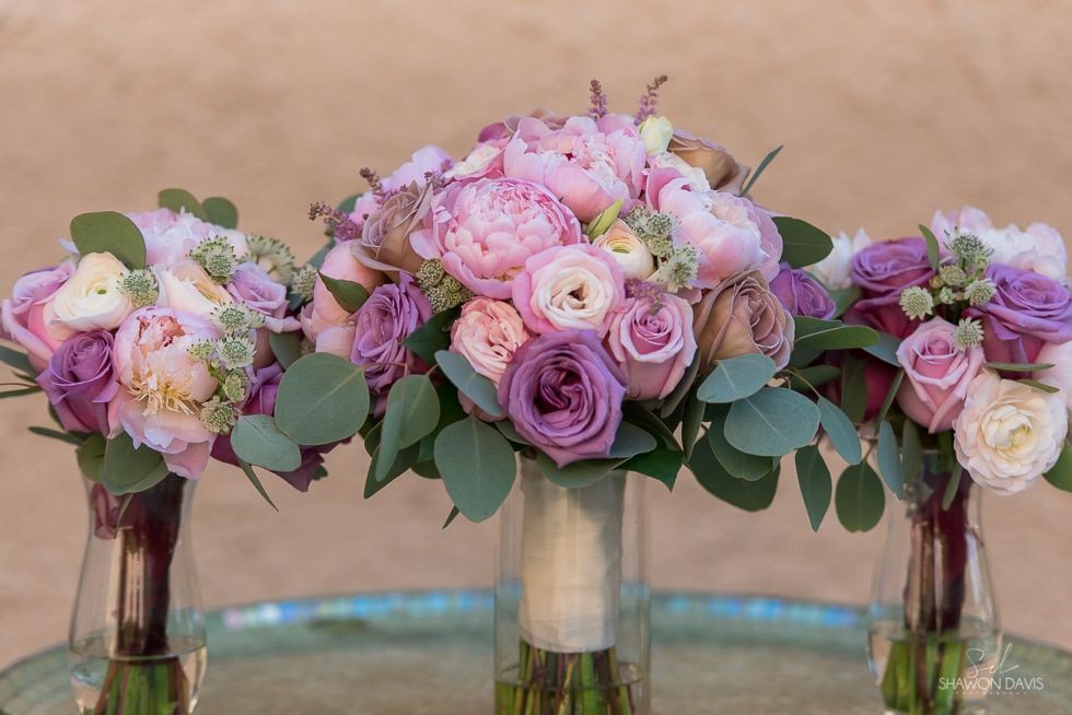 Three pastel floral arrangements in glass vases with pink, lavender, and green blooms