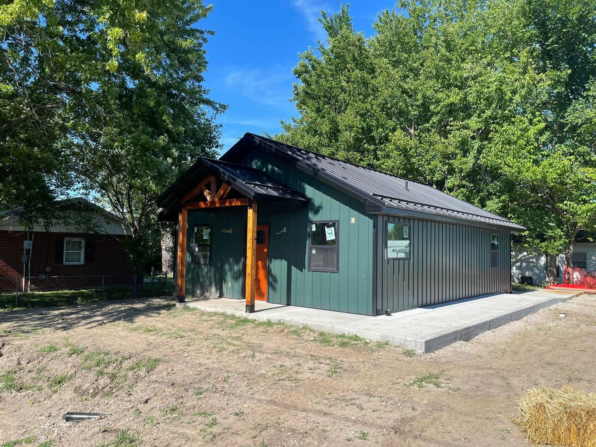 Green cabin with wood posts, metal roof, on concrete slab, under blue sky.