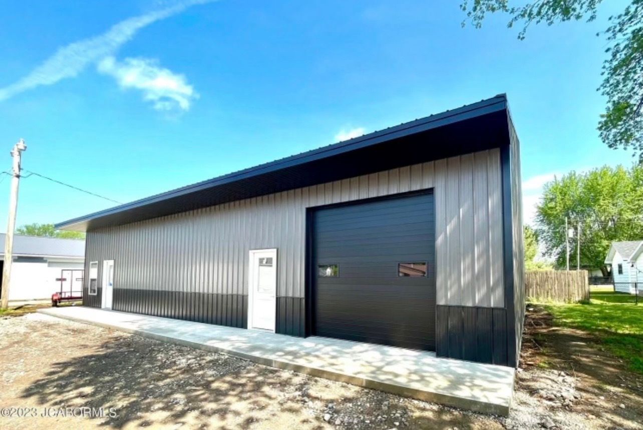 A large metal building with a black garage door is for sale.