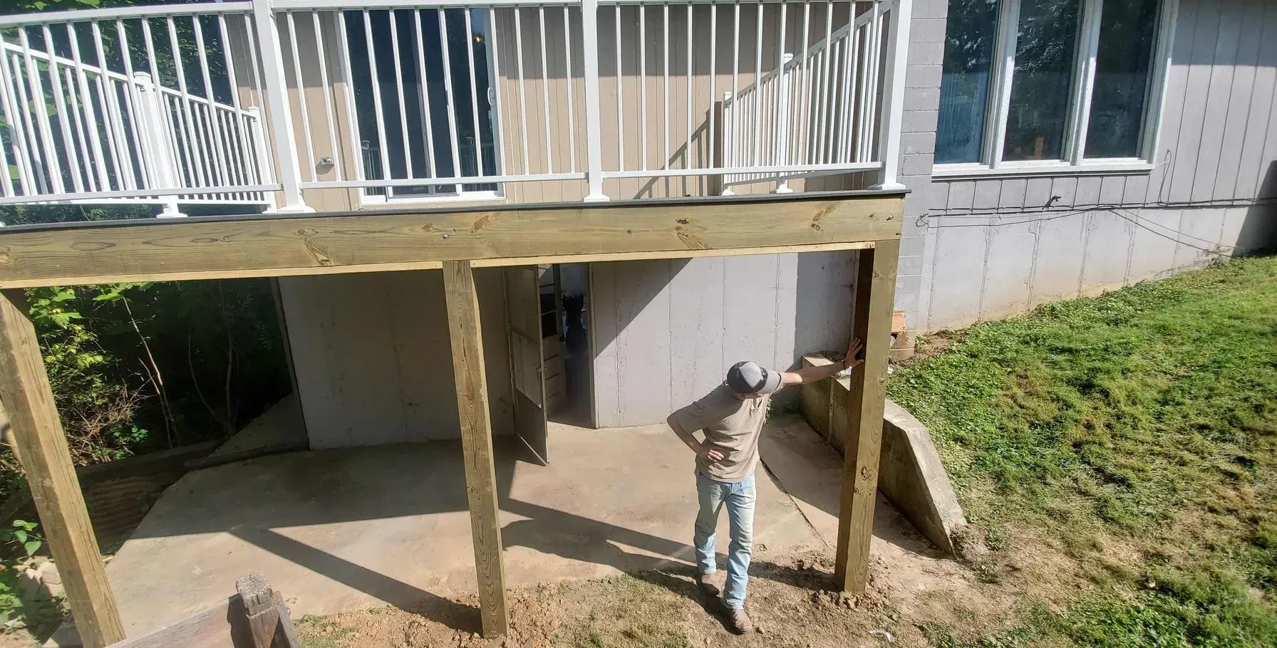 A man is standing under a wooden deck in front of a house.