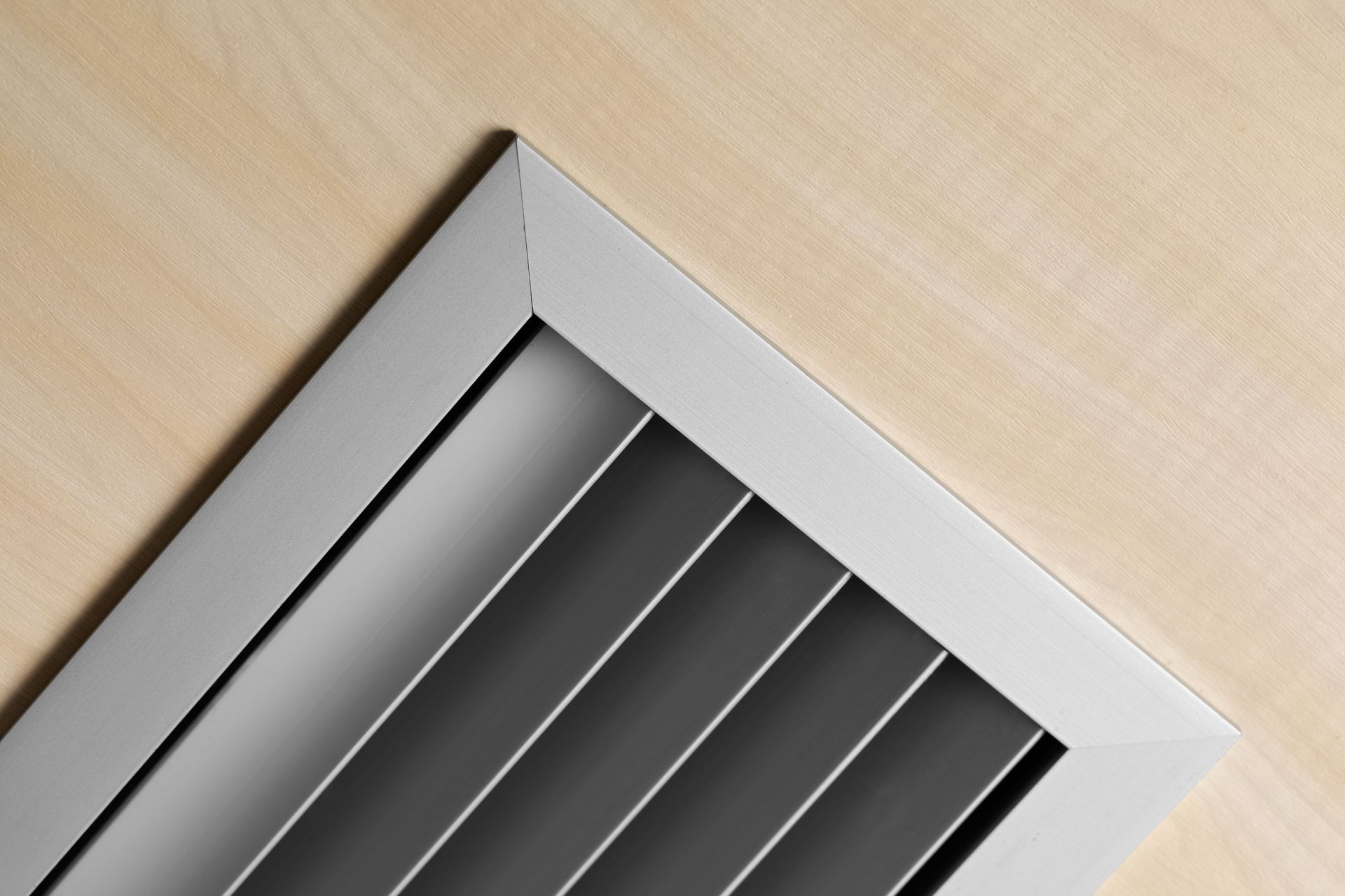 Close-up of a silver metal ventilation grille set into a light wood panel ceiling.