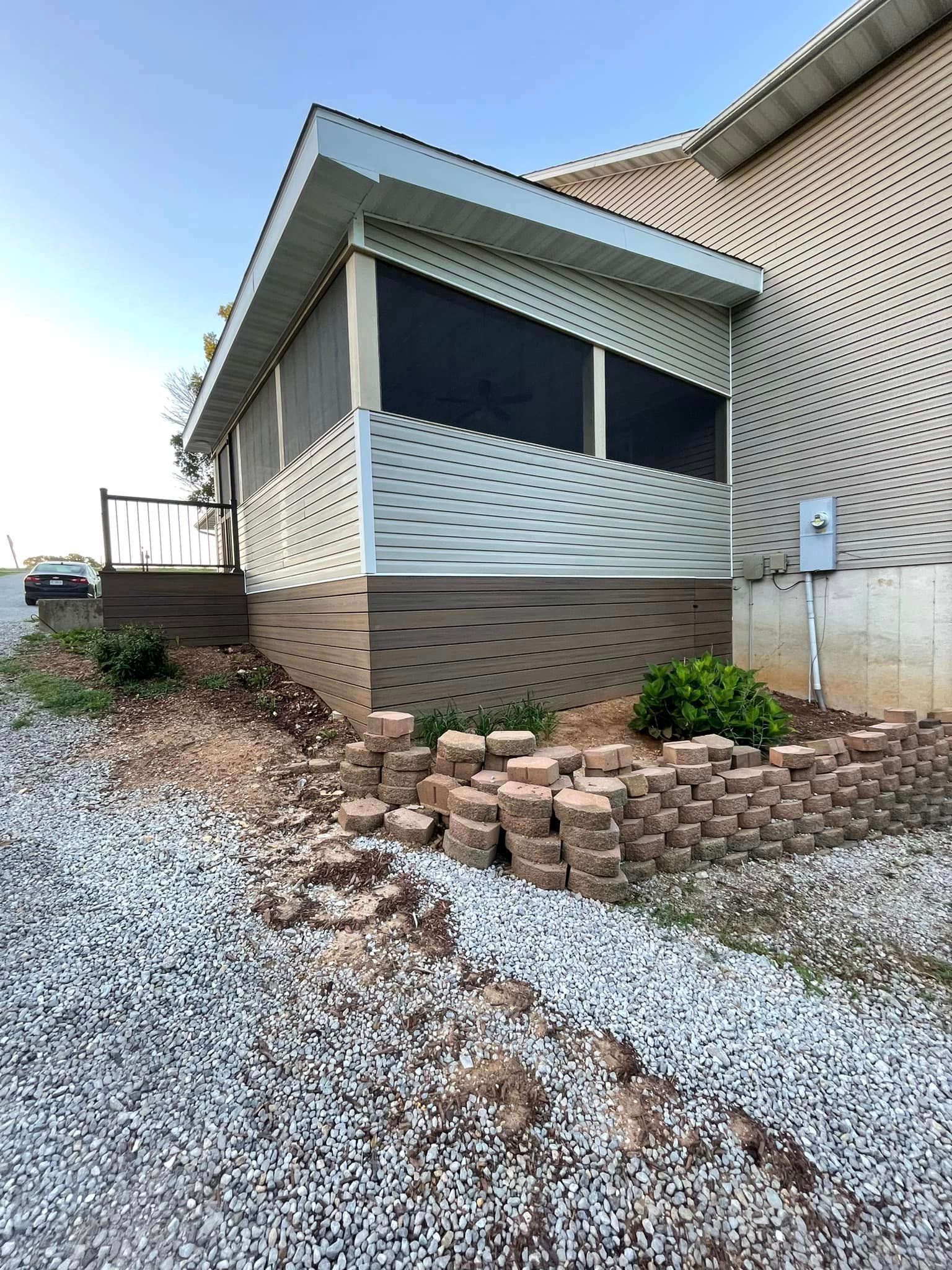 A mobile home with a screened in porch and a gravel driveway.