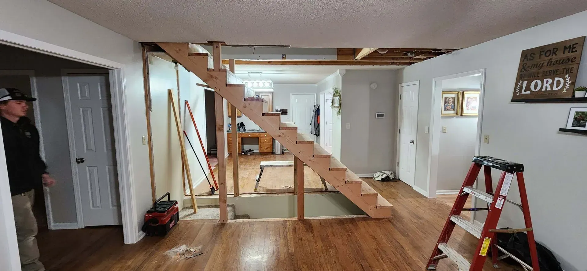A man is standing in a living room next to a wooden staircase being built.