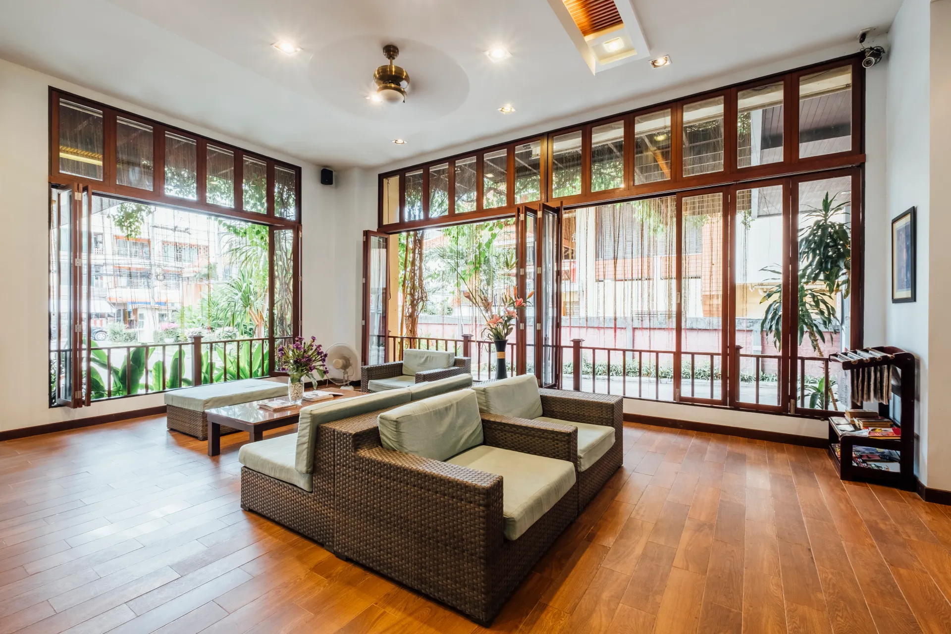 Bright living room with large windows, wooden floors, and green sofas overlooking a balcony