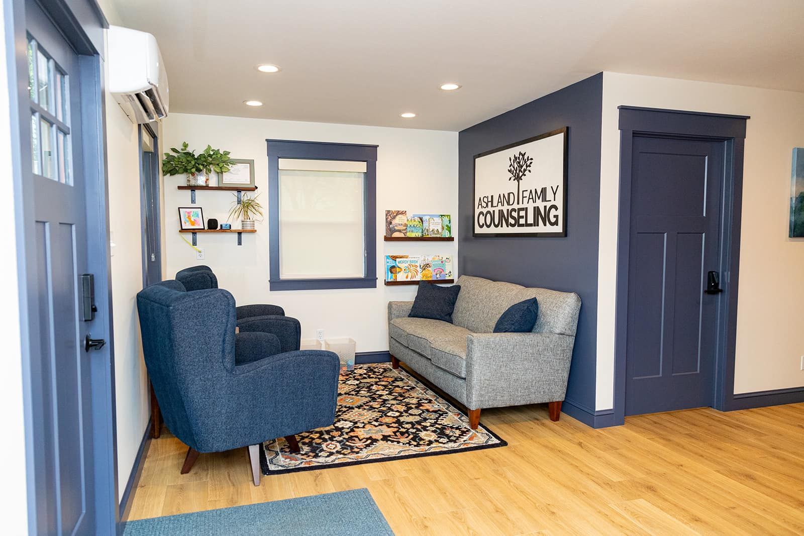 Waiting room with blue and grey furniture, wood floors, and decorative shelves.