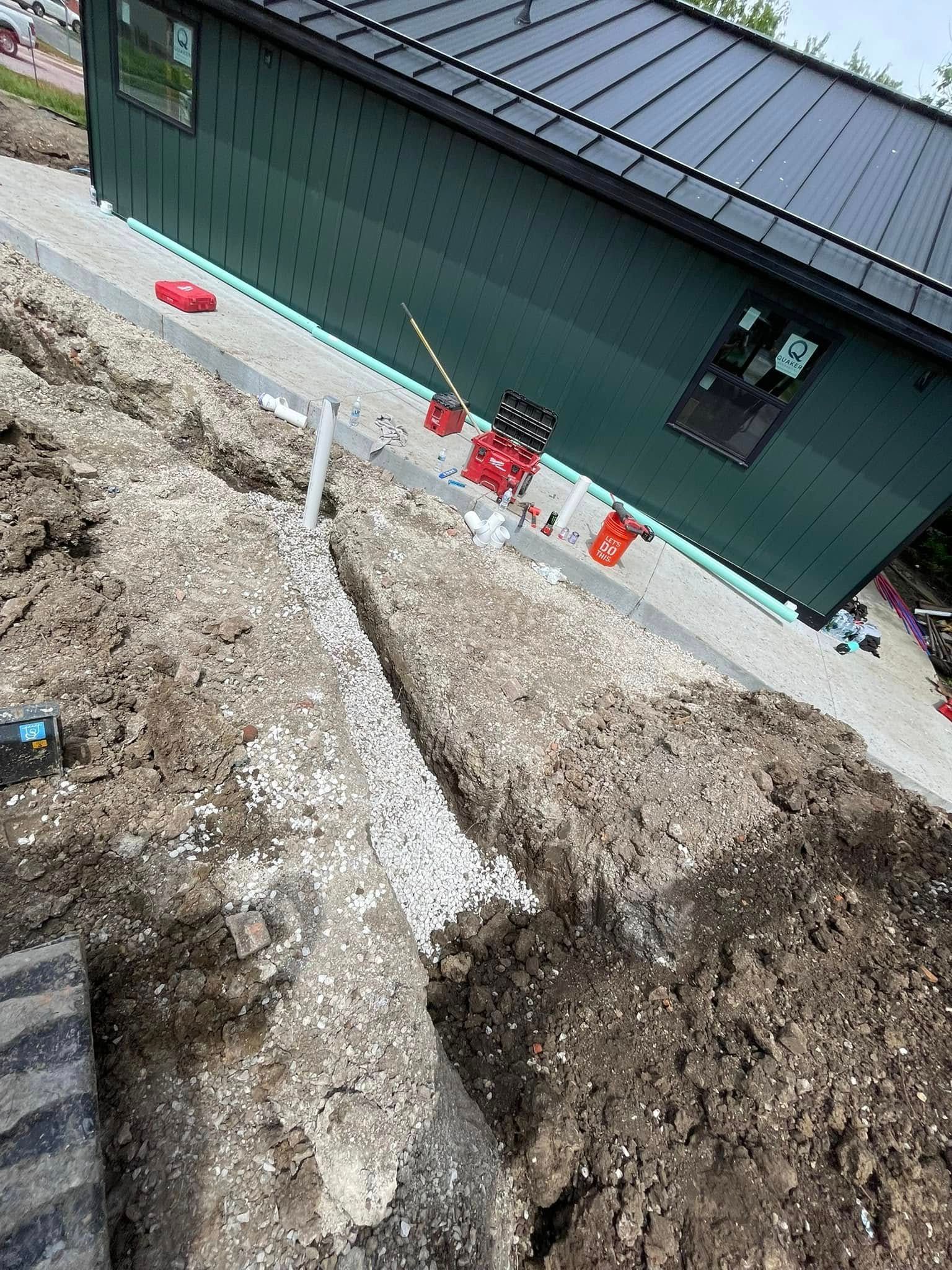 Construction site beside green house with dirt piles and red safety buckets along the foundation