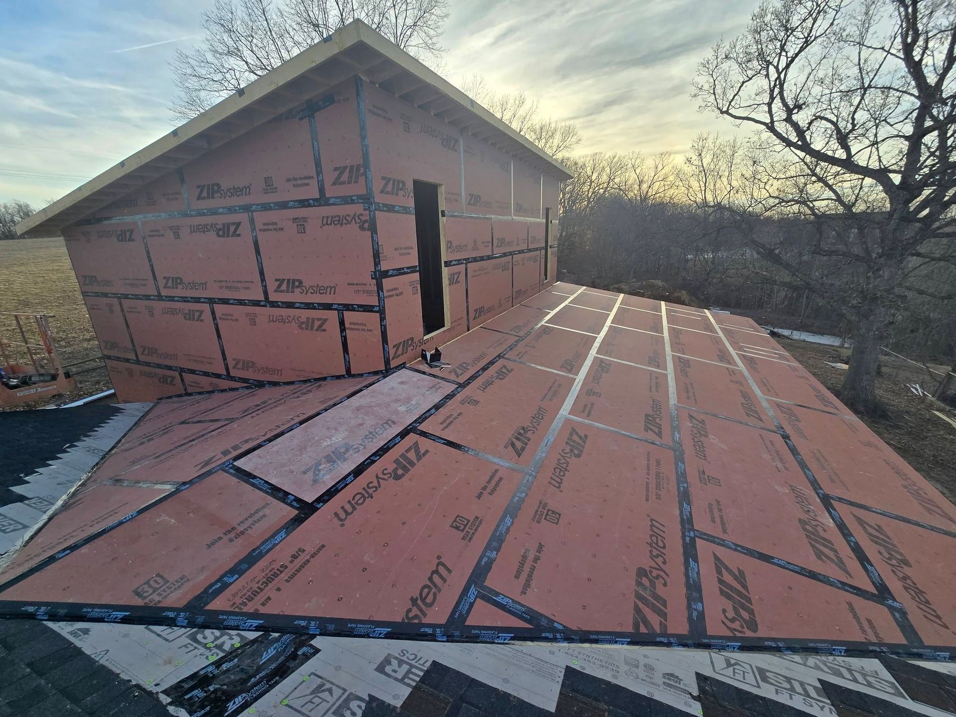 A partially constructed shed with orange sheathing and black sealant; outdoors.