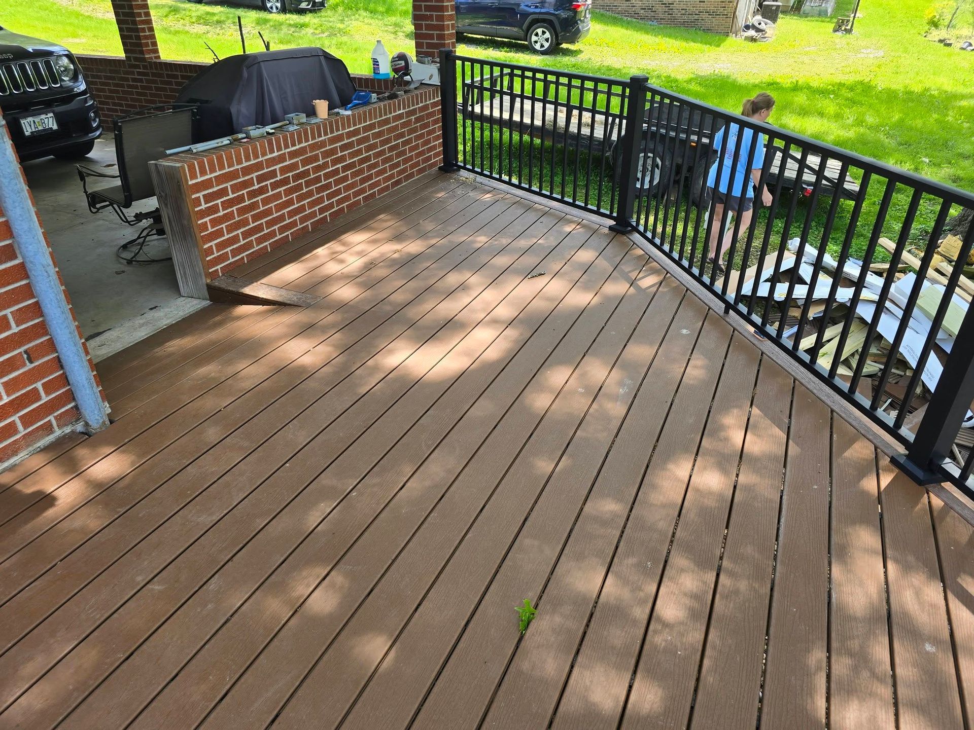 Composite deck with black railing and brick wall. Person in blue shirt standing on deck.