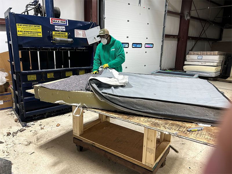 A man wearing a mask is working on a mattress in a factory.