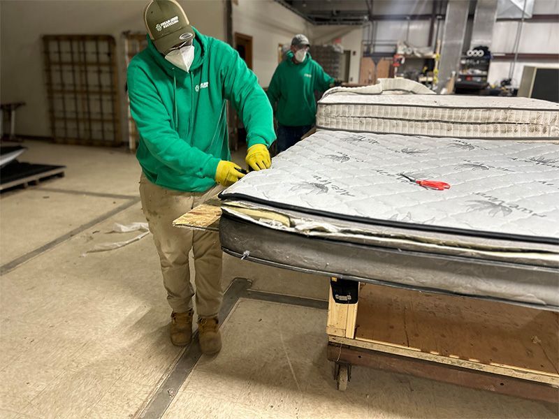 A man in a green jacket is working on a mattress in a factory.