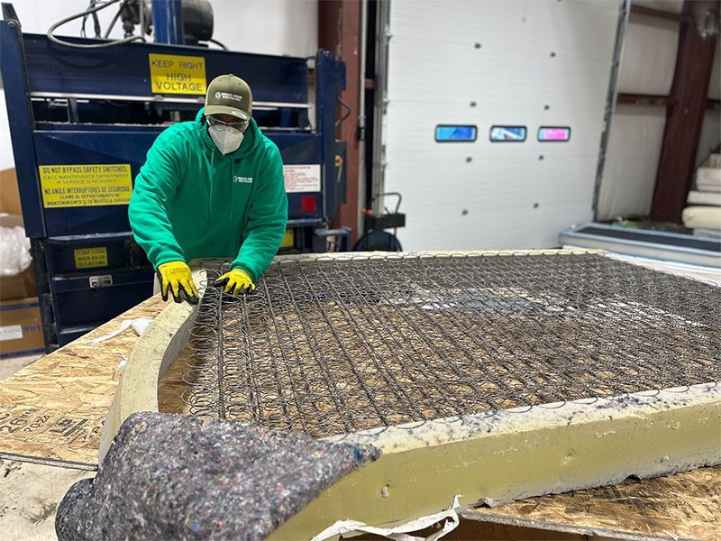 A man wearing a green jacket and yellow gloves is working on a mattress.