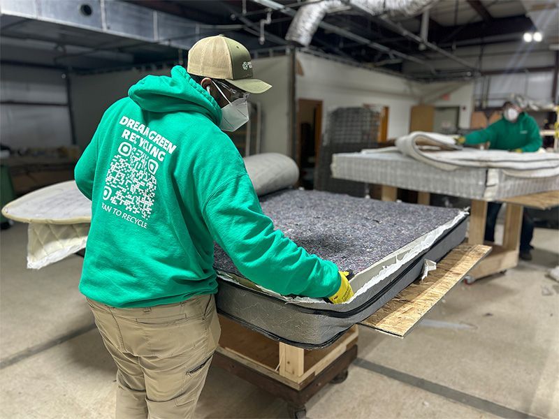 A man in a green hoodie is working on a mattress in a factory.