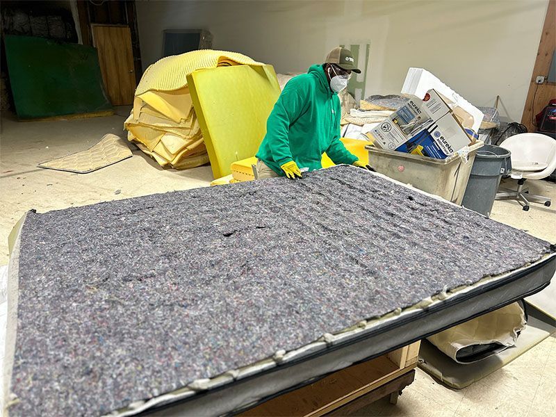 A man wearing a mask is working on a mattress in a room.