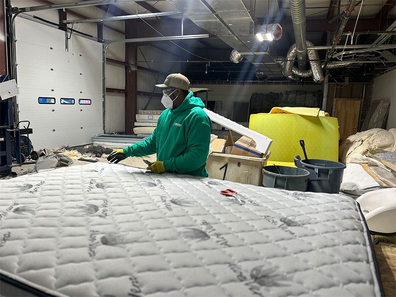 A man wearing a mask is working on a mattress in a factory.