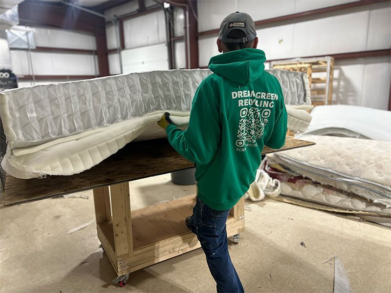 A man in a green hoodie is holding a mattress in a room.