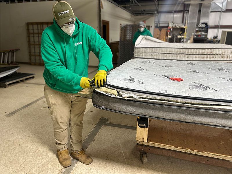 A man in a green hoodie is working on a mattress in a factory.