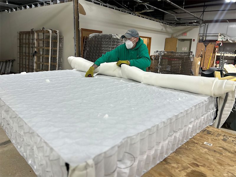 A man wearing a mask is working on a mattress in a factory.