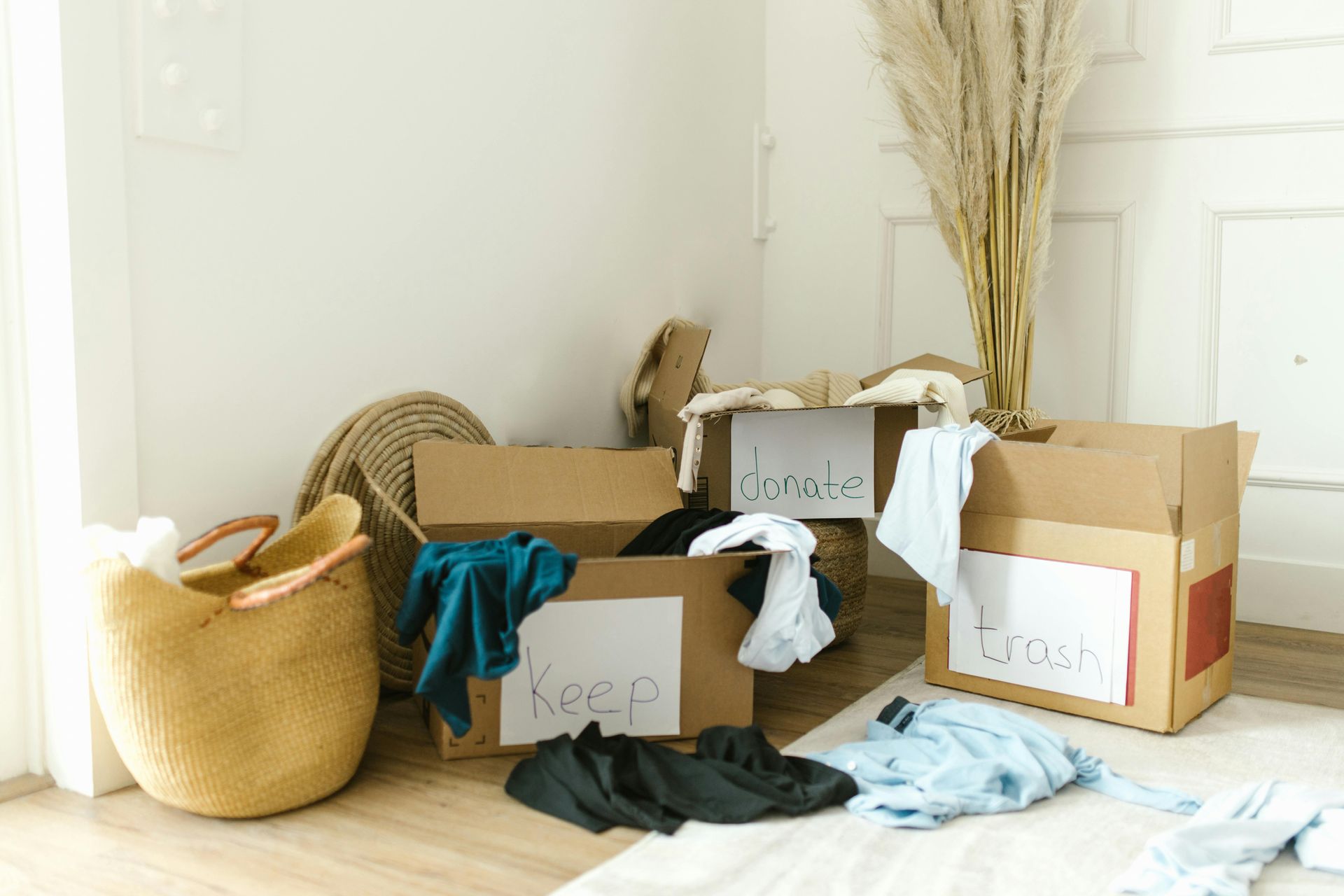 A room filled with cardboard boxes filled with clothes and a basket.