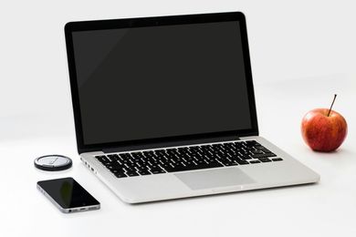 Laptop with a blank screen, smartphone, clock, and red apple on a white surface.