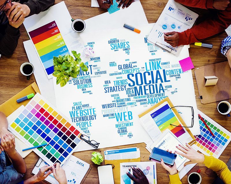 Un gruppo di persone è seduto attorno a un tavolo con documenti e un cartello che dice social media.