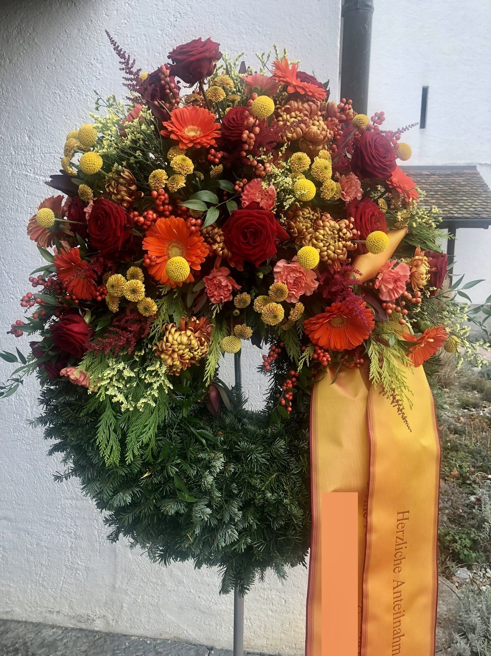 Blumenkranz orangefarbene Bänder und Koniferen