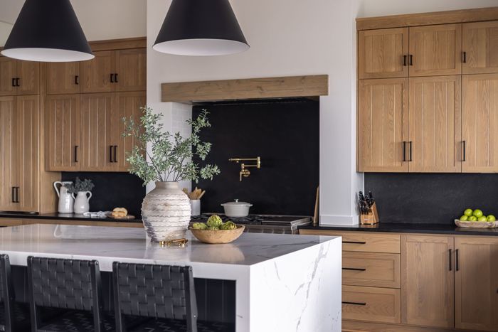 Modern kitchen with wood cabinets, black backsplash, white countertop island, and black pendant lights.