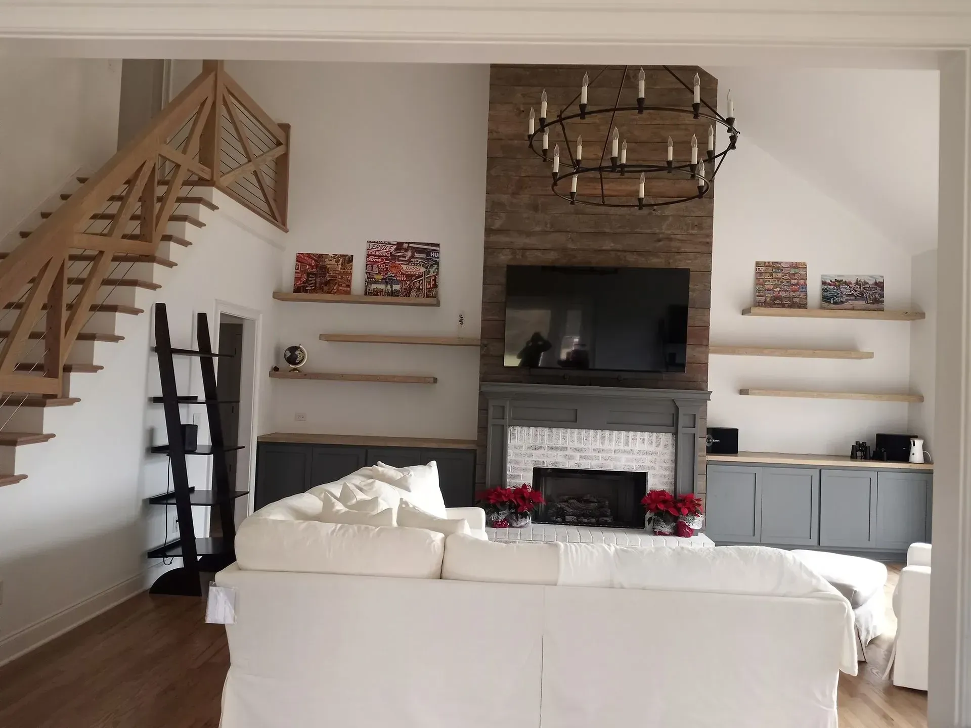 Living room with white sofa, fireplace, floating shelves, and wooden staircase.