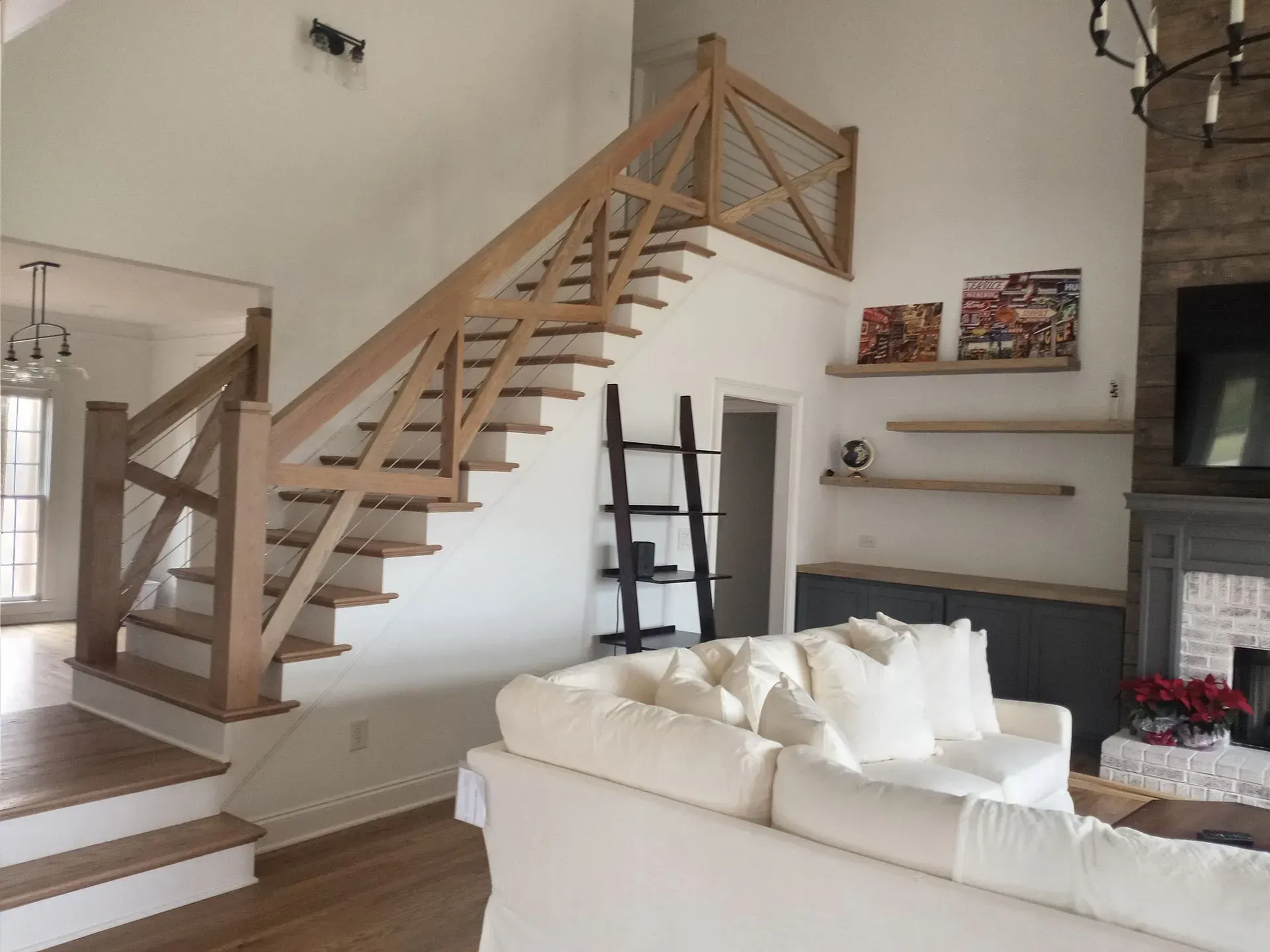 Wooden staircase in a bright, modern living room with a white couch and floating shelves.