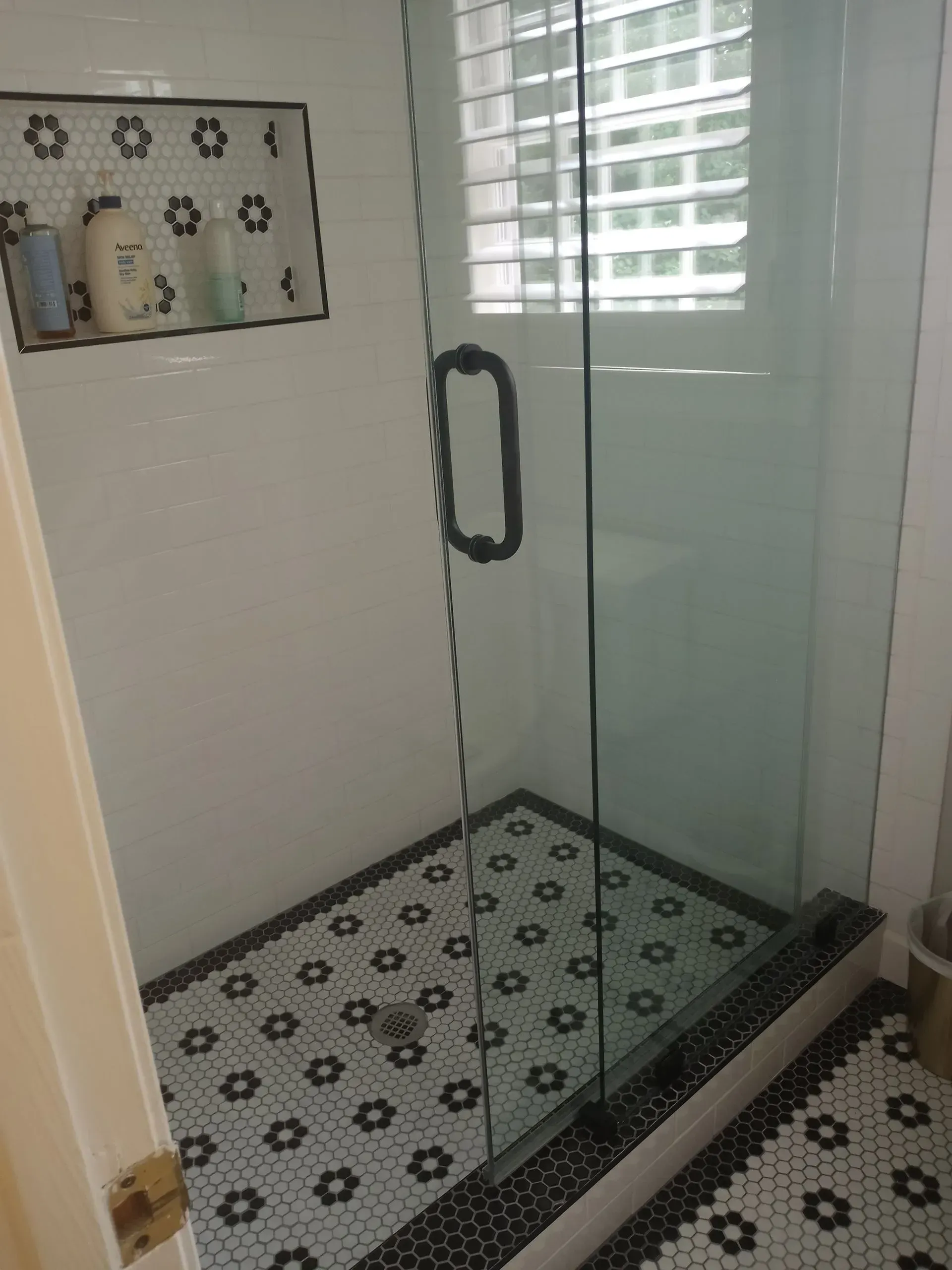 Shower with white and black floral tile floor and a glass door.