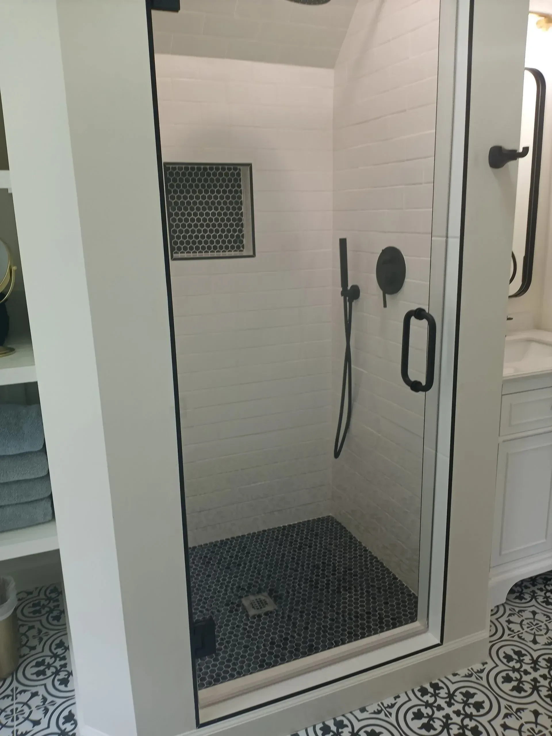 Shower with black trim, black hexagon floor tile, and white subway tile walls.