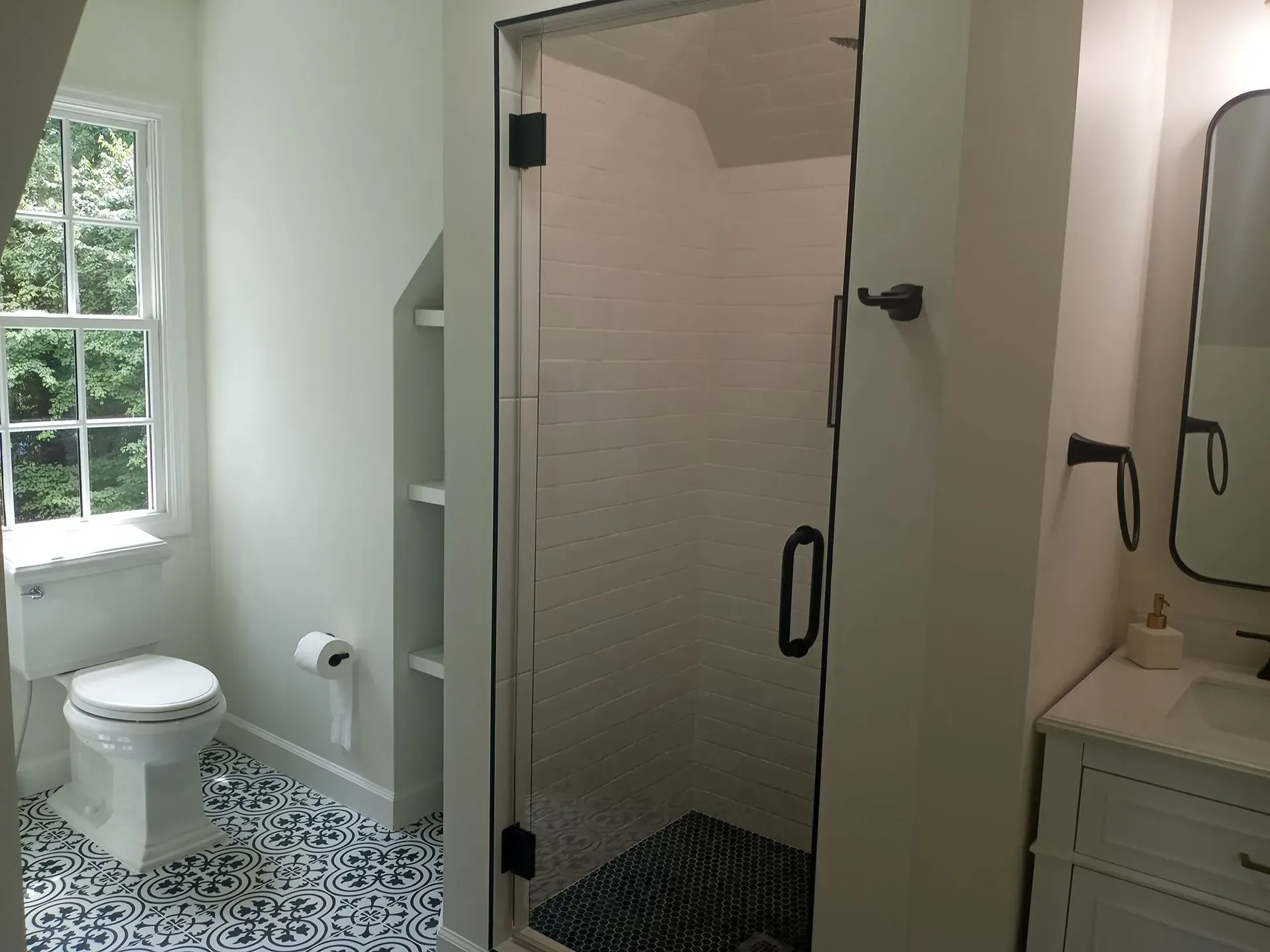 Bathroom with white walls, patterned tile floor, glass shower door, and toilet.