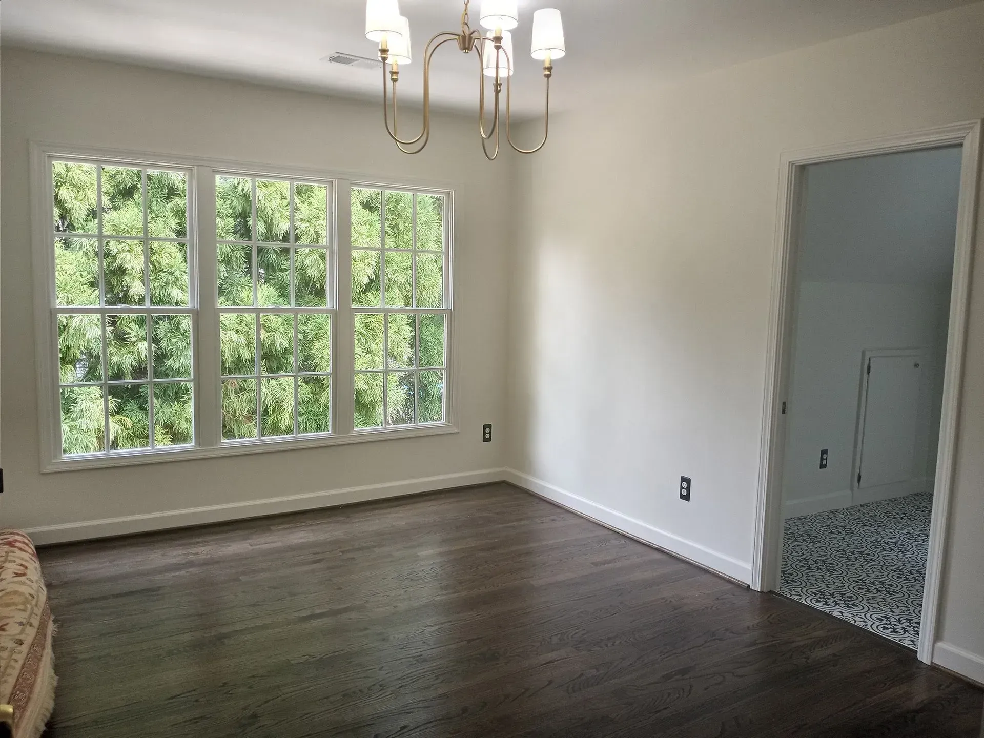 Empty room with hardwood floors, large windows, chandelier, and doorway.
