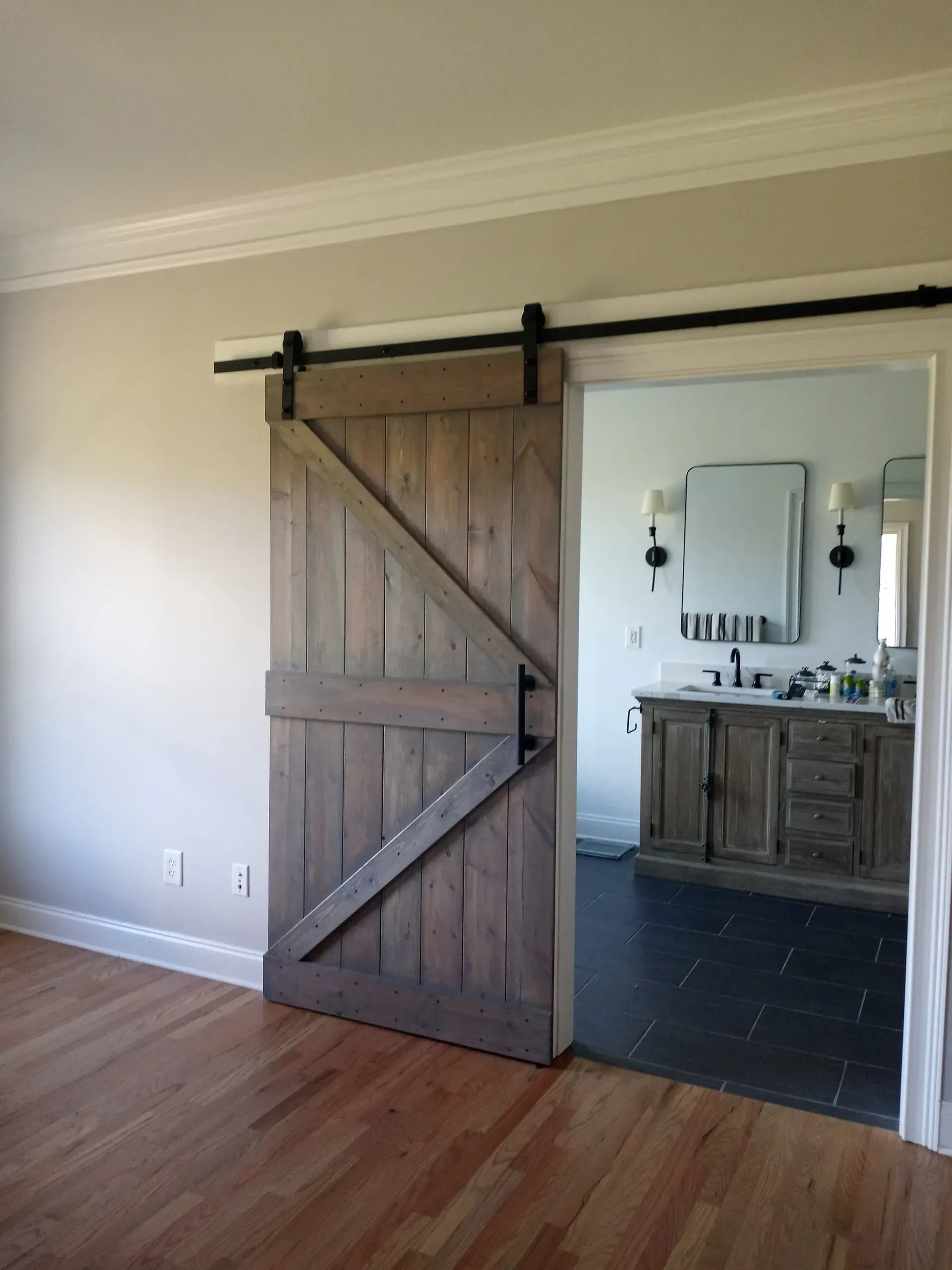 Wooden barn door on black track partially covering bathroom entrance.