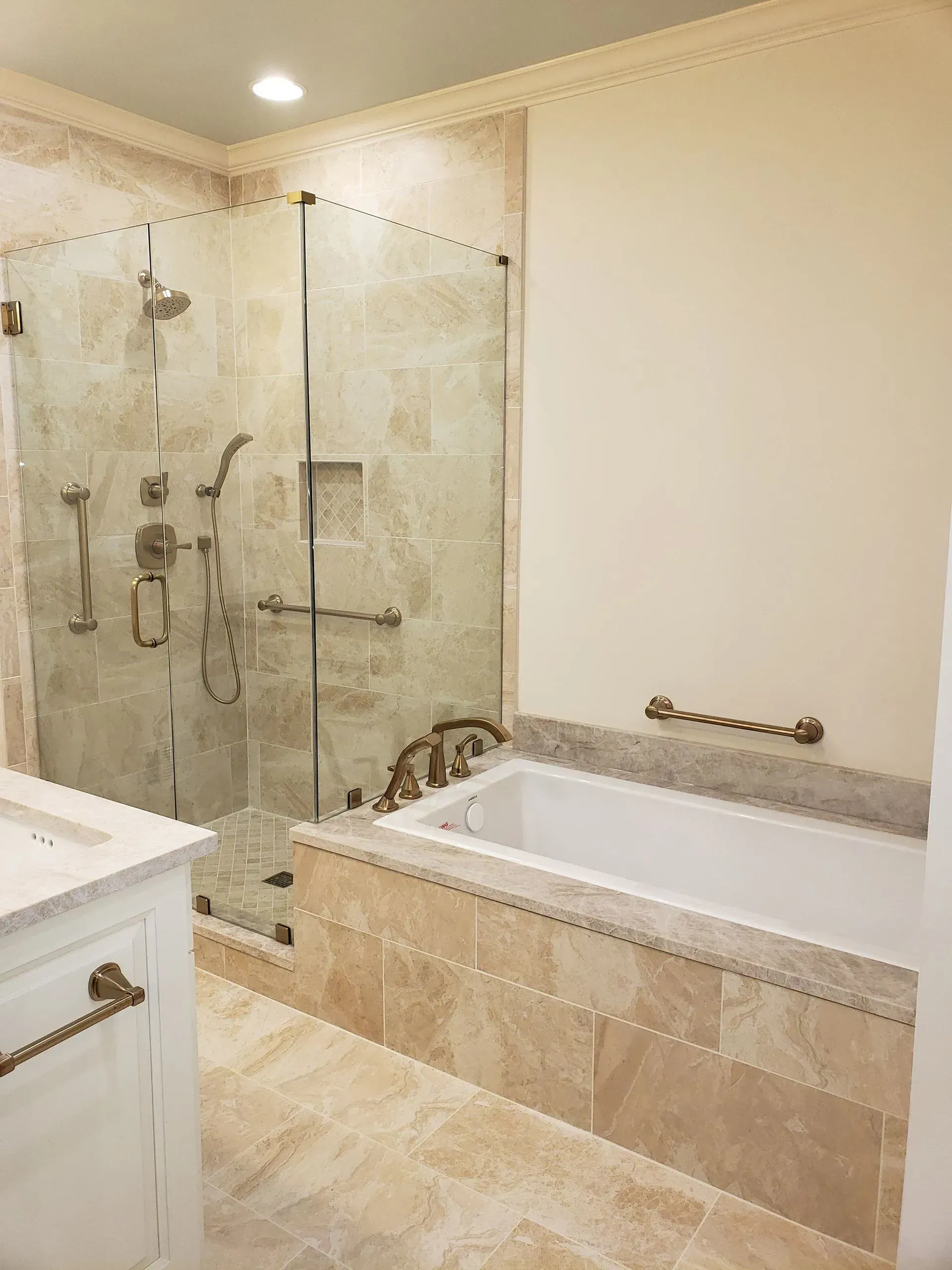 Bathroom with a tiled shower and a built-in bathtub, cream-colored walls, and gold fixtures.