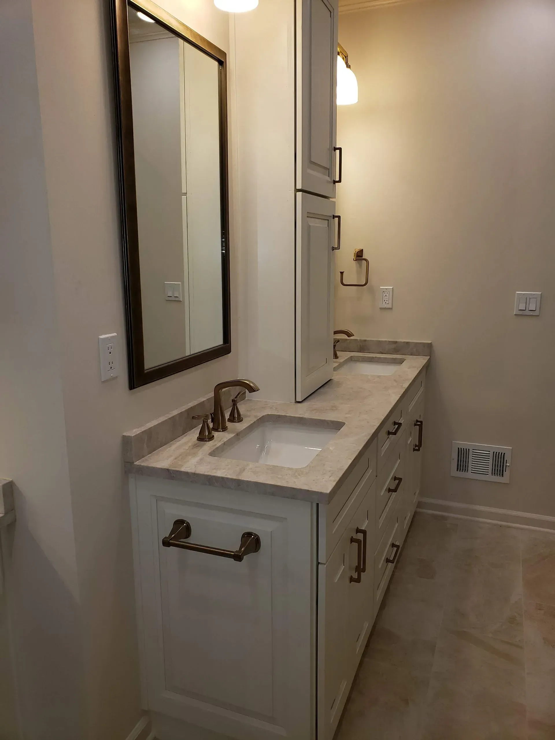 Bathroom with white vanity, marble countertop, dual sinks, gold fixtures, and tall storage cabinet.