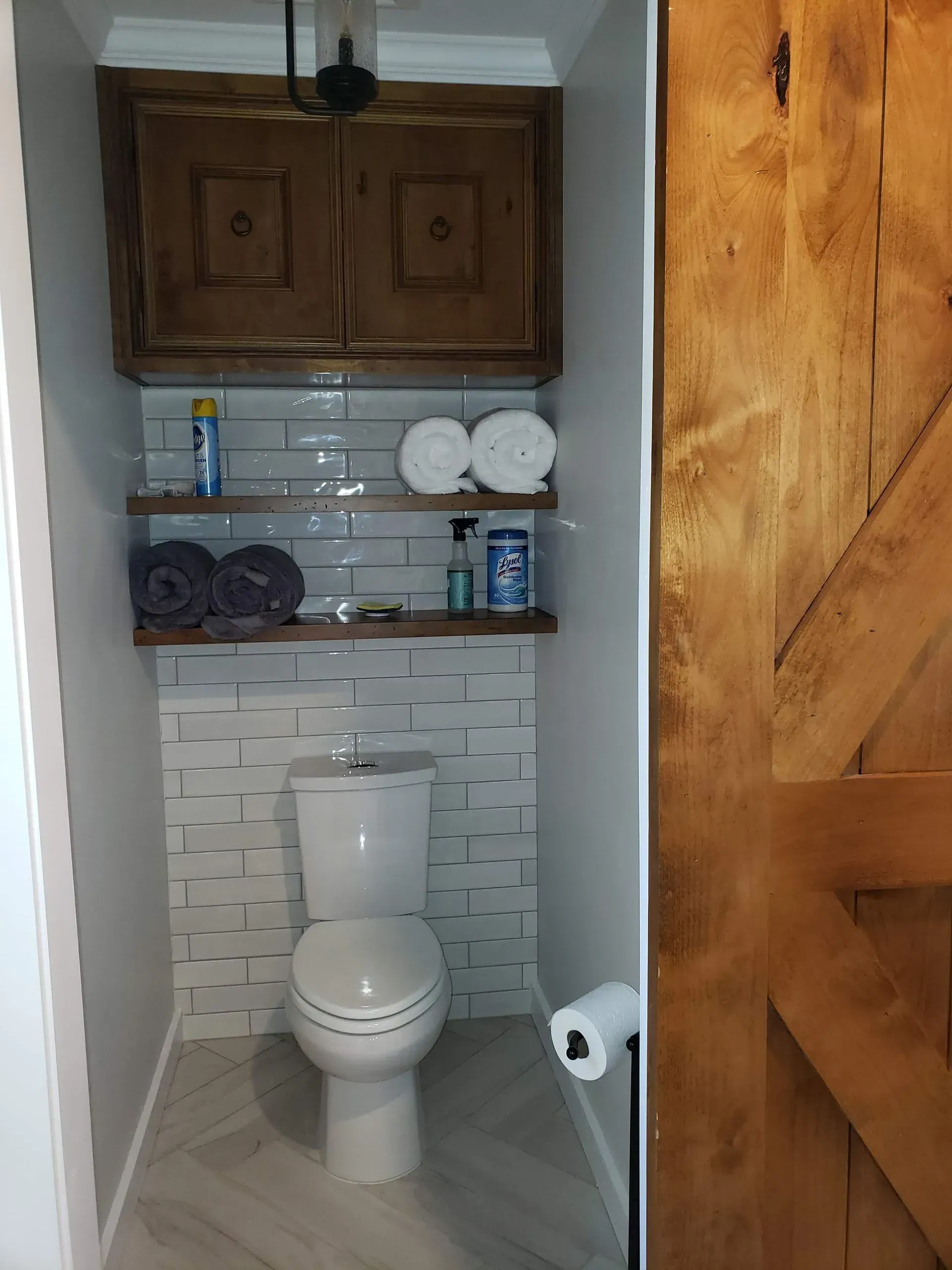 Small bathroom with white toilet, wood shelves, and a barn door.