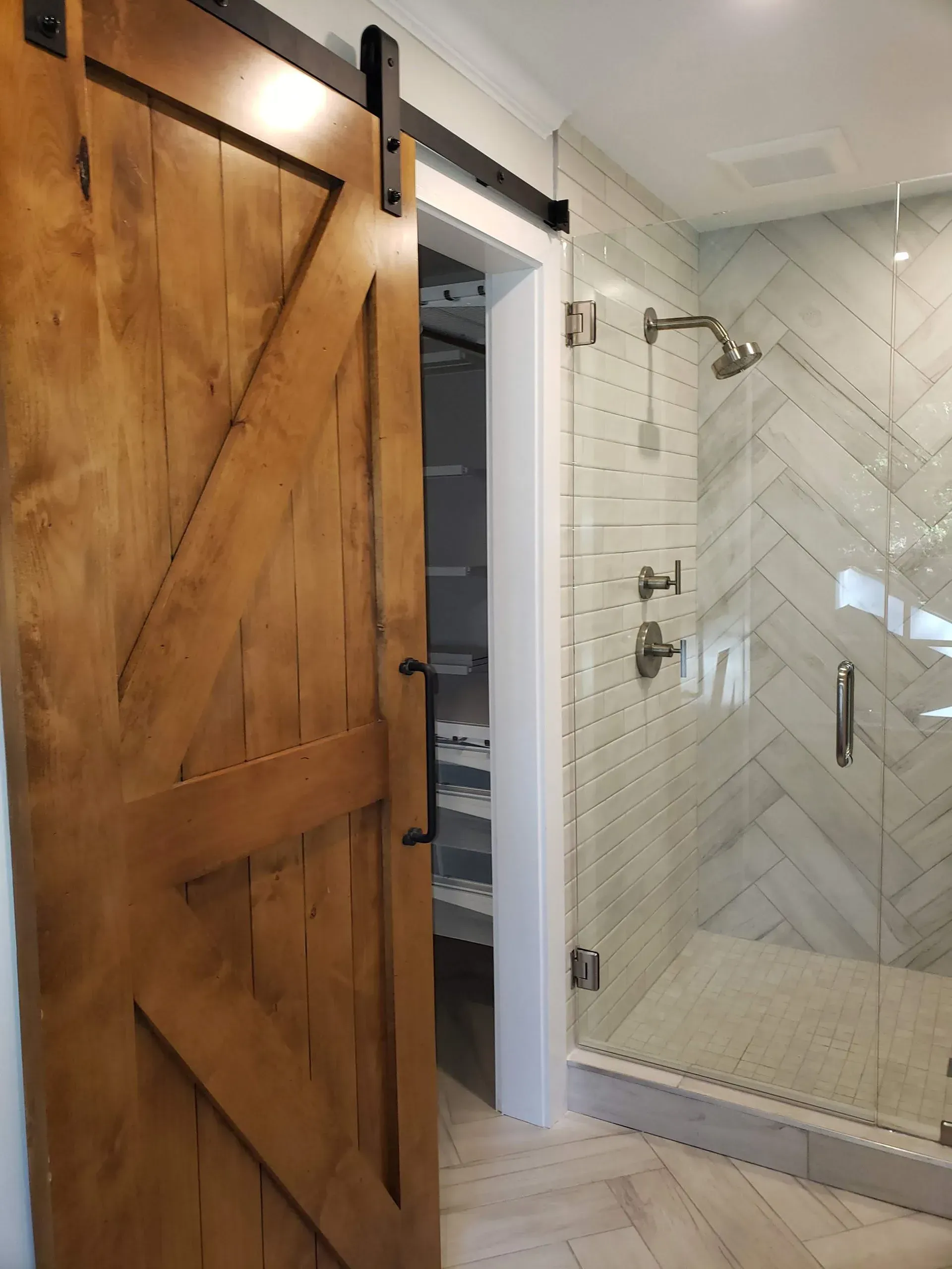 Barn door leading to a closet, next to a shower with white and gray tiled walls and glass doors.