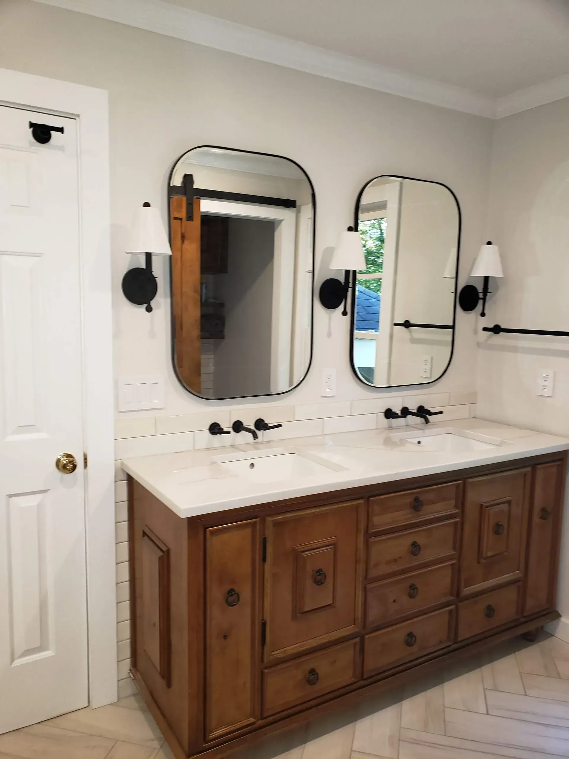 Bathroom vanity with two mirrors, black sconces, a wooden cabinet, and white countertops.