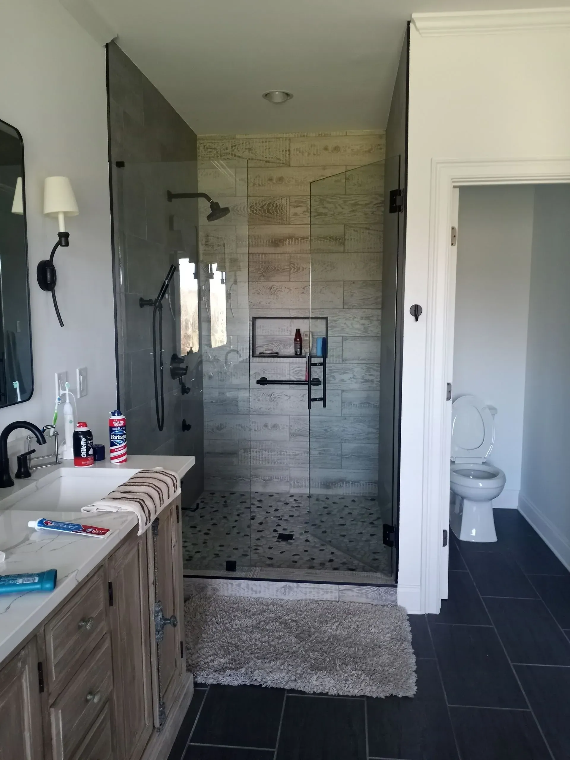 Bathroom with a walk-in shower. Gray and white tile, glass doors, and a wood vanity are featured.