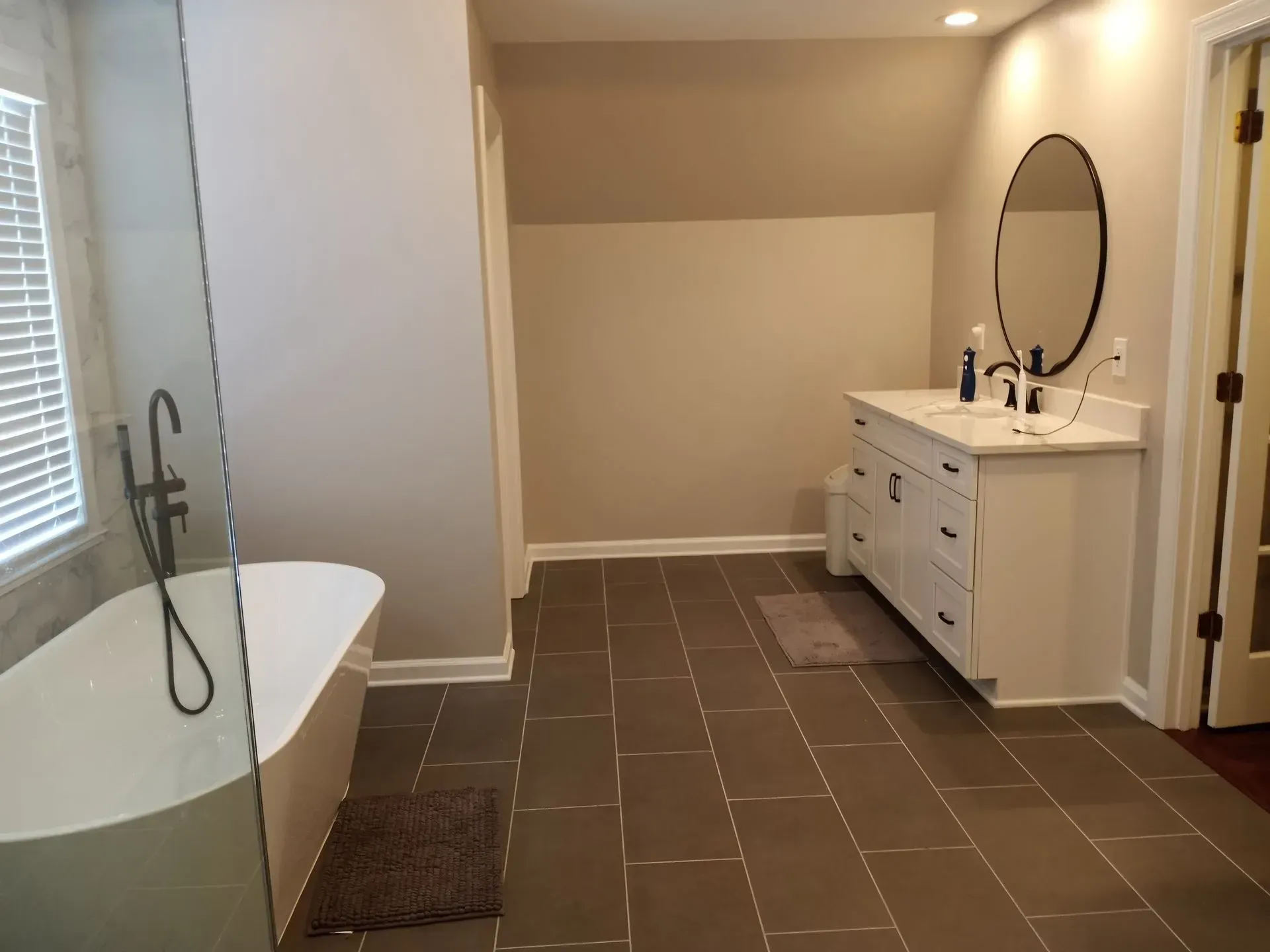 Bathroom with a white freestanding tub, white vanity, and gray tile floor.