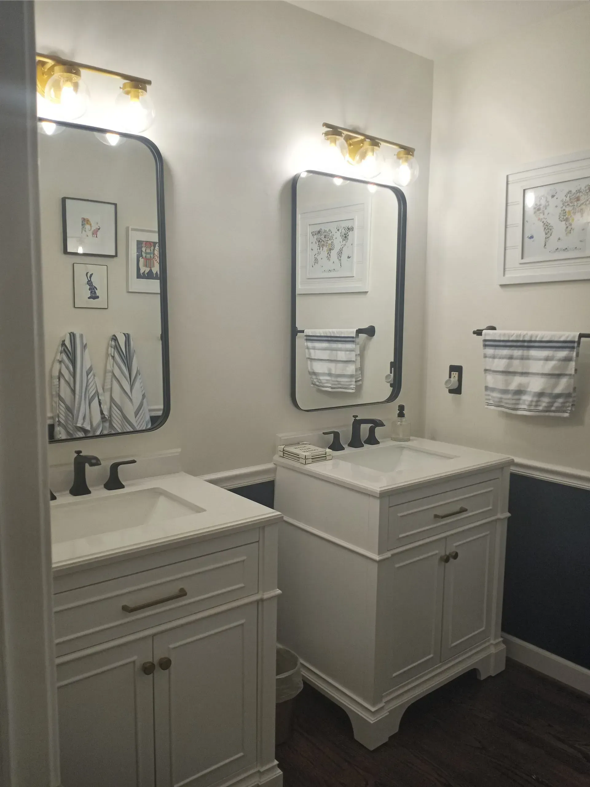 Two white vanities with black framed mirrors, gold lights, and framed artwork in a bathroom.