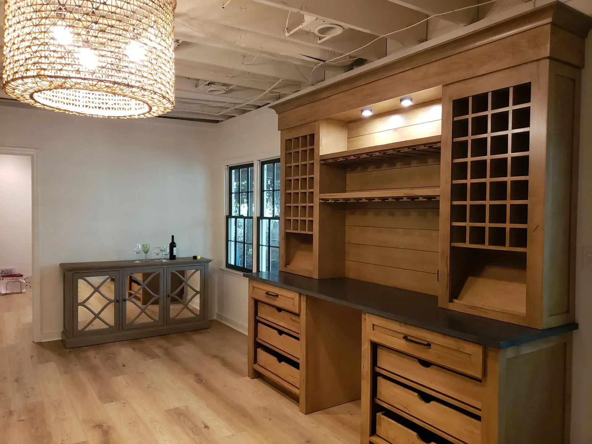 Wine storage and serving area with wooden cabinetry and a light fixture.