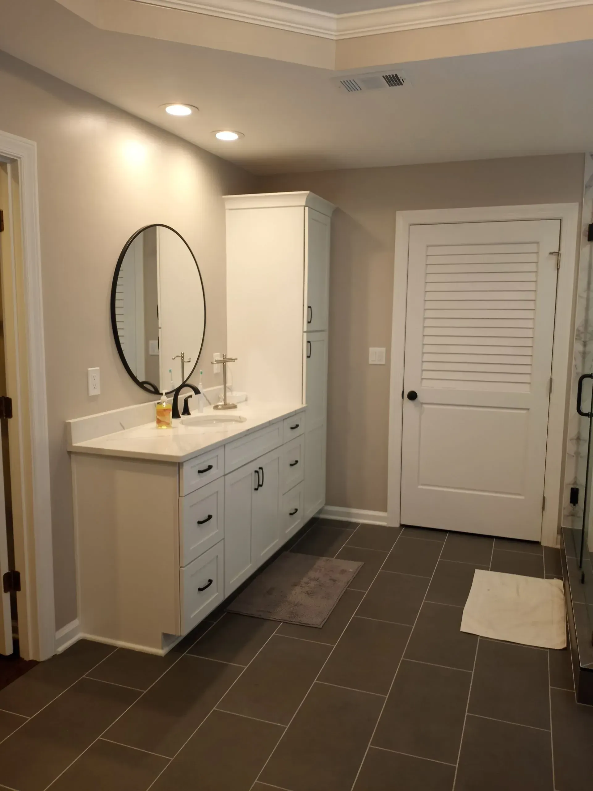 Bathroom with white cabinets, oval mirror, gray floor tiles, and a white door.