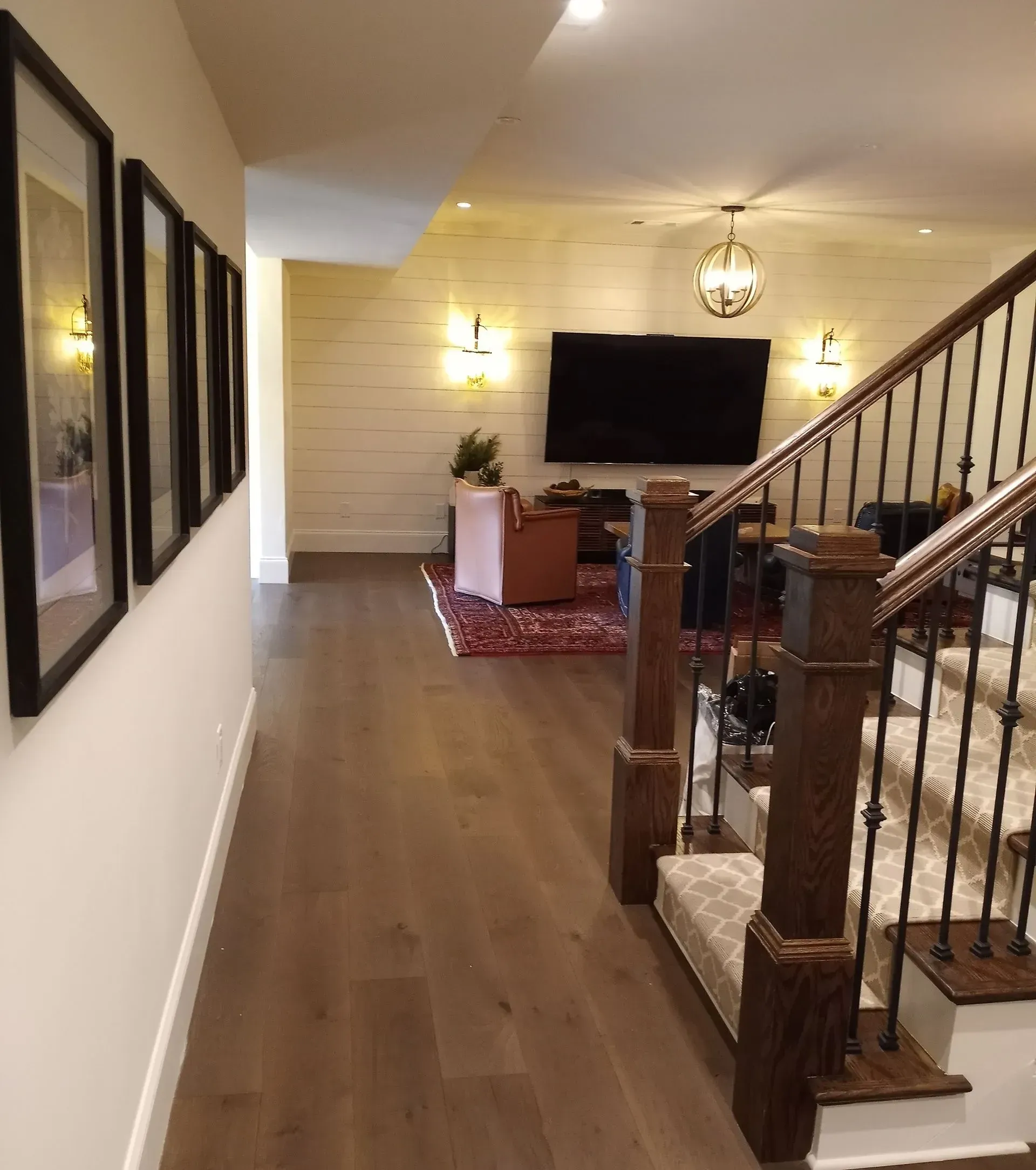 Hallway with wood floors, stairs on the right, and a living room with a TV and wall sconces.