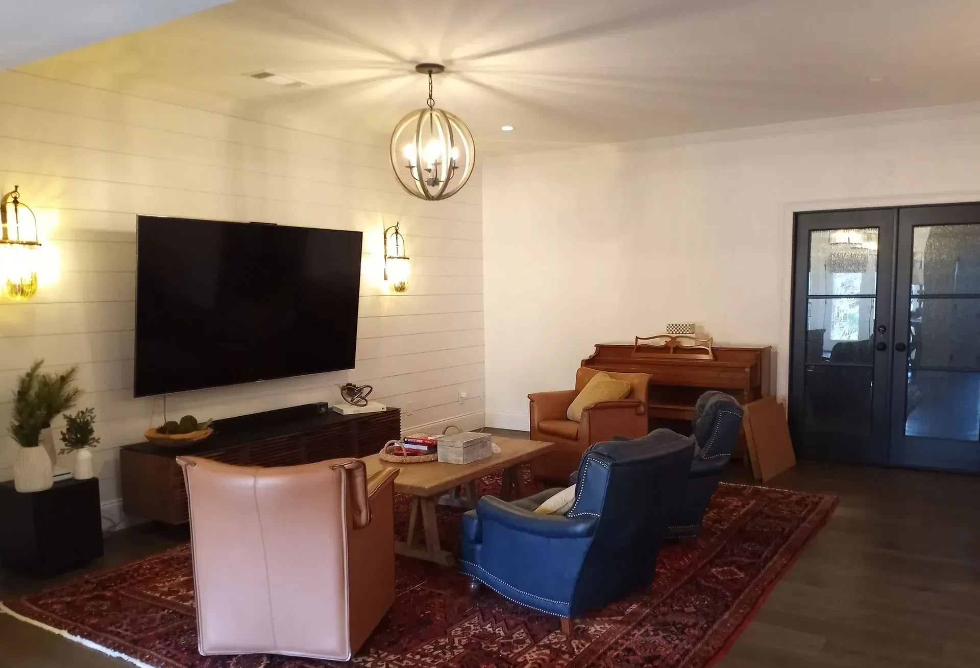 Living room with TV, chairs on a rug, fireplace, chandelier, and french doors.